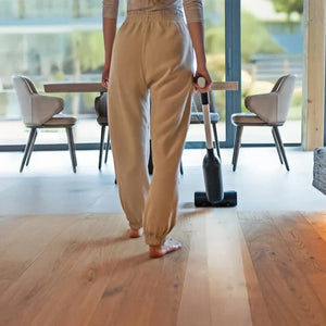 Person cleaning a wood floor with a cordless vacuum cleaner in a modern living room